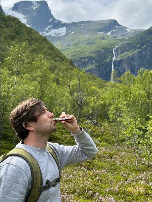 Man drinkt een collageen shot tijdens een wandeling in de natuur met bergen op de achtergrond.