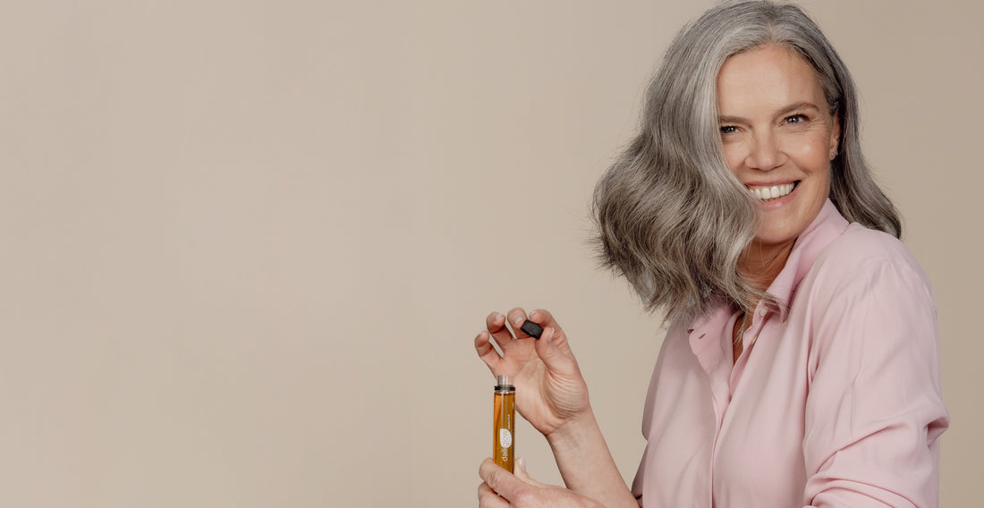 Vrouw met grijs haar glimlacht terwijl ze een vloeibaar voedingssupplement in een ampule vasthoudt.