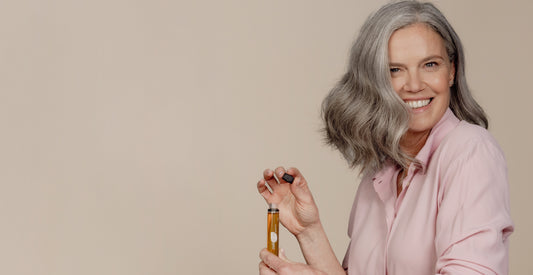 Vrouw met grijs haar glimlacht terwijl ze een vloeibaar voedingssupplement in een ampule vasthoudt.