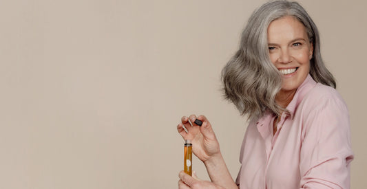 Vrouw met grijs haar glimlacht terwijl ze een vloeibaar voedingssupplement in een ampule vasthoudt.