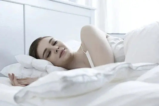 Vrouw slaapt comfortabel in bed, ter illustratie van de rust en het herstel van een vaste slaaproutine en een consistent dagelijks slaapritme.