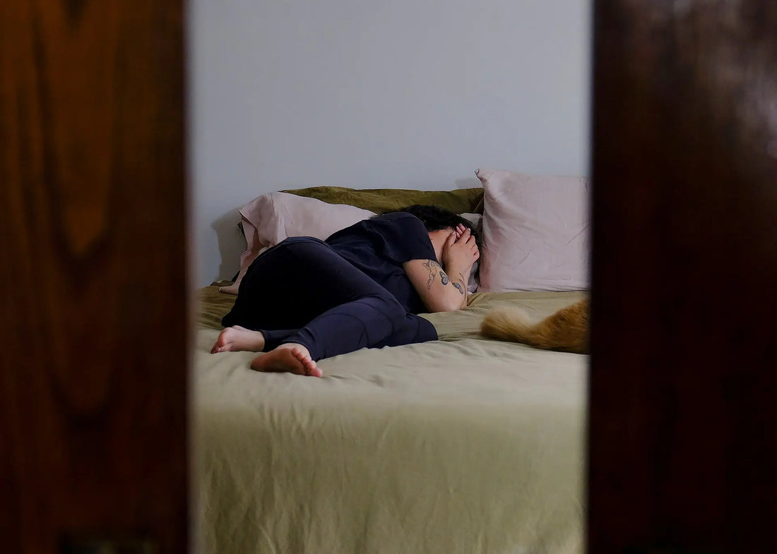 Persoon ligt ’s nachts wakker in bed, opgerold op een laken, wat onrustige slaap en nachtelijk ontwaken symboliseert.