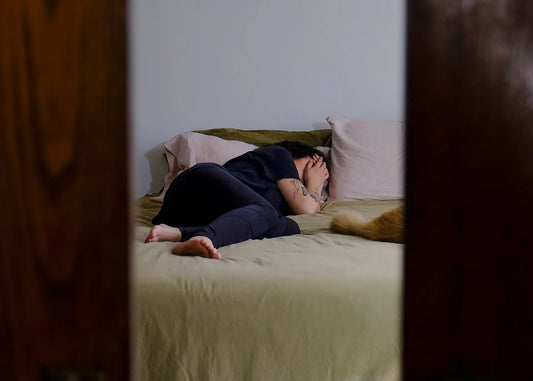 Persoon ligt ’s nachts wakker in bed, opgerold op een laken, wat onrustige slaap en nachtelijk ontwaken symboliseert.