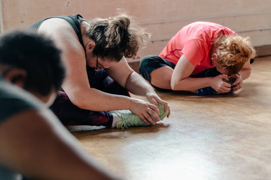 Vrouwen die na een trainingssessie rustige rekoefeningen doen op de vloer, gericht op spierherstel en ontspanning.